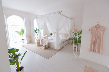Cozy interior of a bright Balinese-style apartment with white walls, bamboo furniture. bed room with night lights, bed with balanchin and large windows