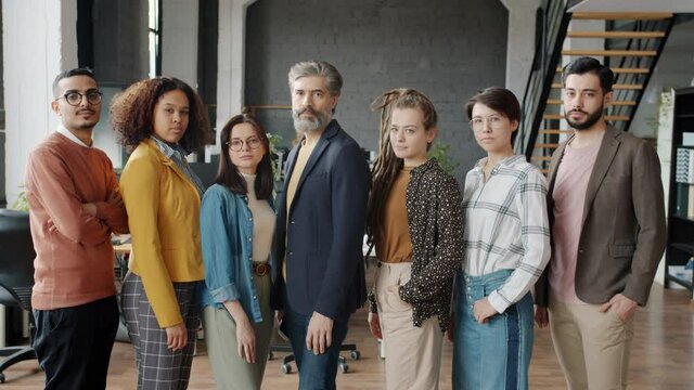 Portrait Of Multi-ethnic Team Men And Women Standing In Open Plan Office And Looking At Camera With Serious Faces. Coworking And People Concept.