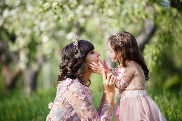 Obraz premium Mother and little daughter hugging each other and walking in blooming apple garden. Mom loves her child. Spring story. Family look romantic similar dresses. Happy family in beautiful spring day