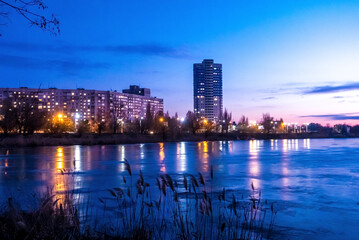 Evening city donwtown landscape with sunset, electric lights and frozen lake. Kharkiv, Ukraine