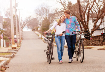 Beautiful young couple walk with bicycles together down the street hugging and smiling