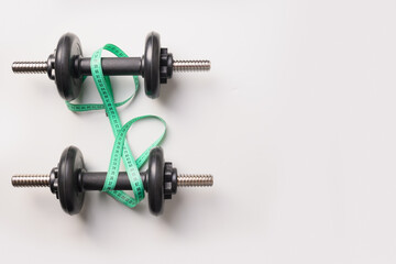Sport dumbbells and green measuring tape on grey background. View from above. Space for text.