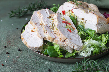 Turkey breast stuffed with vegetables and cheese served with green mix salad and aromatic herbs, green stone background.