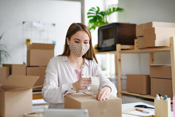 Woman dropshipper working at home, packing parcels. Coronavirus concept.