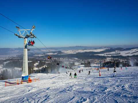 Ski slope, chairlift, skiers and snowboarders in Bialka Tatrzanska ski resort in Poland in winter. Snow cannons in action