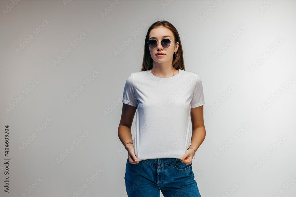 Poster Stylish girl in glasses wearing white t-shirt posing in studio