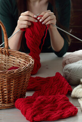 Young woman knitting red muffler at home in leisure time, fancywork and needlework concept, closeup of hand work, copy space, from above overhead view