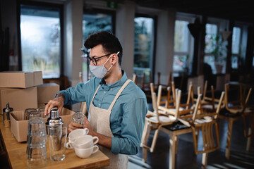 Frustrated waiter packing glasses in closed cafe, small business lockdown due to coronavirus.