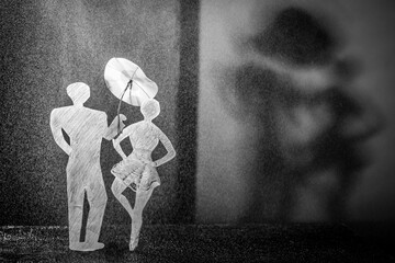 Monochrome still life: paper figures of people. A man holds an umbrella over the girl's head, protecting her from the rain.