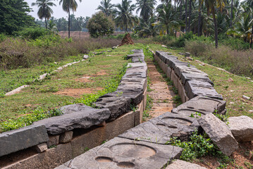Fototapeta na wymiar Hampi, Karnataka, India - November 5, 2013: Ancient Aqueduct. closeup of section flowing through green landscape with imprinted border stones. 