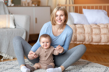 Fototapeta premium Mother playing with her infant child, sitting on bed