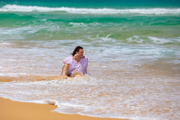 Fototapeta na wymiar A man with long hair is sitting on the beach in the sea.