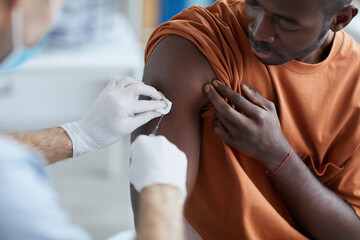 Close up of unrecognizable male nurse injecting vaccine in shoulder of African-American man during...