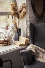 Home interior. Old chair and a mirror on the brick wall. Books and a plaster bust on the windowsill.