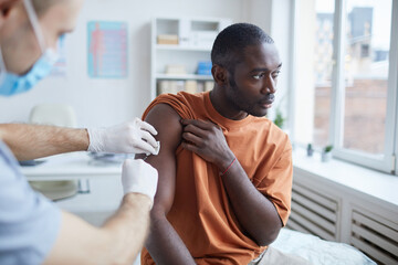 Portrait of adult African-American man looking away while getting covid vaccine in clinic or...