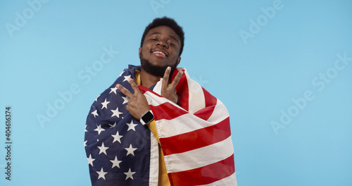 Portrait of African American man with United States of America flag standing isolated over blue background. USA Memorial day and Independence day concept.