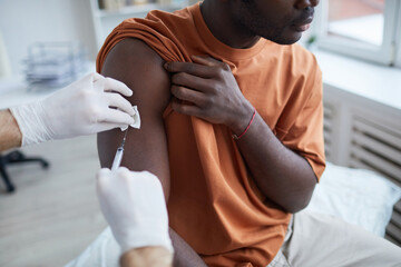 Close up of adult African-American man looking away while getting covid vaccine in clinic or hospital, with male nurse injecting vaccine into shoulder - obrazy, fototapety, plakaty