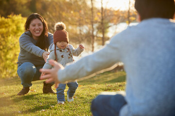 Chinese mother watching young daughter take first steps outdoors.