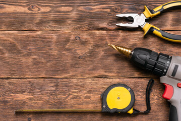 Construction tape, cordless drill and pliers on the brown wooden table background with copy space.
