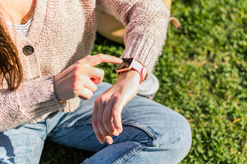 Fototapeta premium Close up of woman's hands checks the time on smart watch sitting in a park