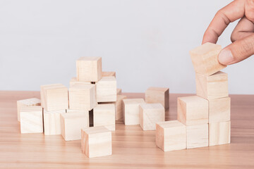 Hand putting and stacking blank wooden cubes on the table with copy space. Hand arranging wood block stacking as step stair. Business concept.