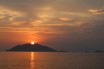 Fototapeta na wymiar Colorful clouds, sunset, sea and island silhouettes. Orange sun on the hill.