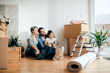 Fototapeta na wymiar Happy parents and daughter moving into their first home and relaxing on the floor. Copy space.