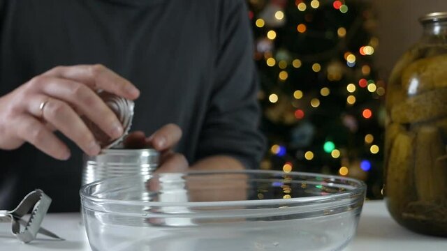 Strong man using opener hands cutting the lid of a metal can on a table with pickles in front of a christmas tree.green peas for traditional salad