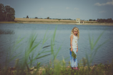 cute child by the river with huge colorful bunch of wild flowers