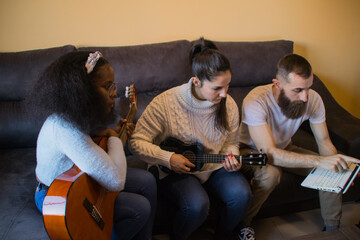 Multiethnic group learning to play the guitar at home with a laptop