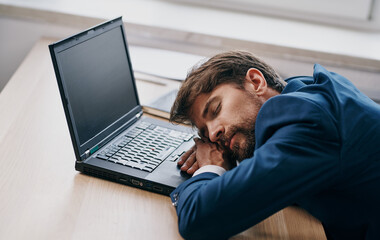 Man in a suit at a working table in front of a laptop office tired