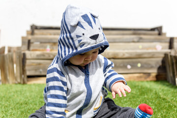 Simpática bebé jugando sentada en el jardin de casa con sudadera