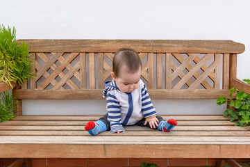 Simpática bebé jugando sentada en banco de madera en jardin de casa con sudadera