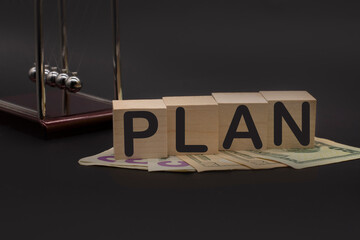 Word plan on wooden cubes, American dollars and Newton's cradle on office desk
