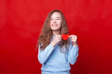 Portrait of little girl holding red paper heard over red background and looking at the camera.