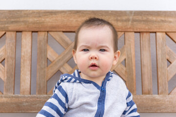 Simpática bebé jugando sentada en banco de madera en jardin de casa con sudadera