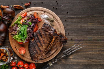 Beef T-Bone steak, herbs and spices on a dark table. Top view. Free space for your text.