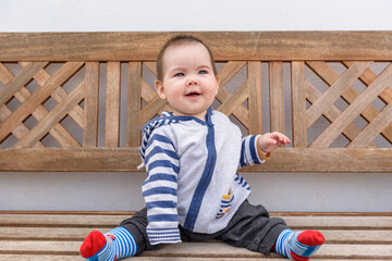 Simpática bebé jugando sentada en banco de madera en jardin de casa con sudadera