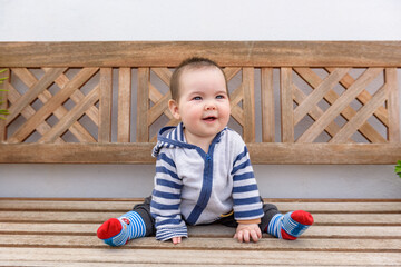 Bebe pequeño chica jugando sentada en banco de madera en jardin de casa con sudadera con capucha