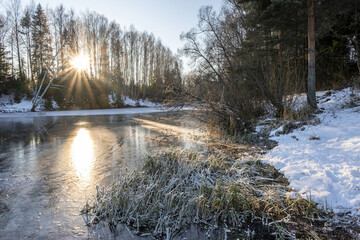 The rays of the low winter sun on the mirror ice of a small backwater.