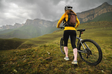 Wide angle bottom view of a young woman sitting on a mountain bike high in the mountains against the backdrop of epic rocks in the evening. Mountain sports bike