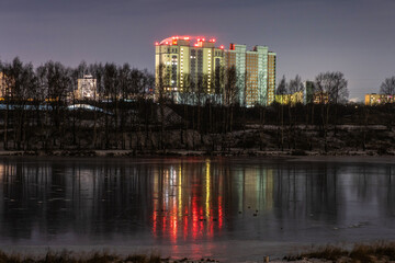 High-rise building on the bank of the river Uvod and its reflection on the mirror ice surface.
