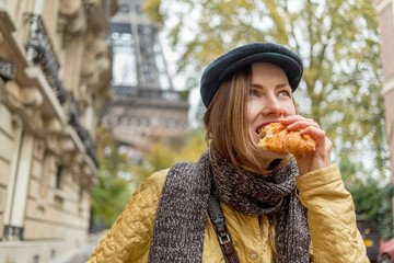 Beautiful woman eating croissant in the street enjoying good warm weather with eiffel tower on the...