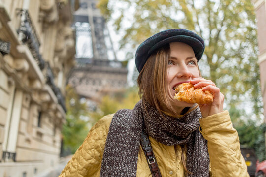 Beautiful woman eating croissant in the street enjoying good warm weather with eiffel tower on the background
