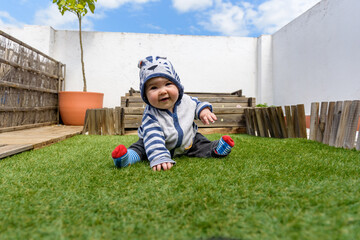 Simpática bebé jugando sentada en el cesped en jardin de casa con sudadera con capucha