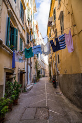 Old narrow street, old residential buildings and washed clothes on a rope in Kerkira, capital of Corfu island, Greece, hot summer day, blue sky.