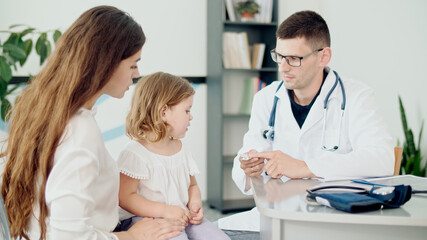 Male Doctor Pediatrician Giving Some Tablets for Ill Kid. Mother With Kid at Visiting Pediatrician. Talking With a Doctor at Consultation During an Appointment.