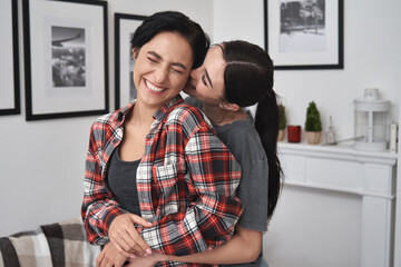 Happy lesbian lgbtq couple in love cuddling, laughing, whispering on ear having fun standing at...