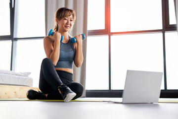 Fototapeta premium asian woman in sportswear is sitting on the floor with dumbbells and using a laptop. sport and recreation concept.