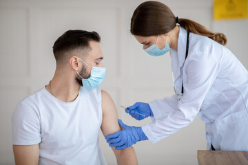 Vaccination against covid-19. Female doctor injecting coronavirus vaccine to male patient's arm at...